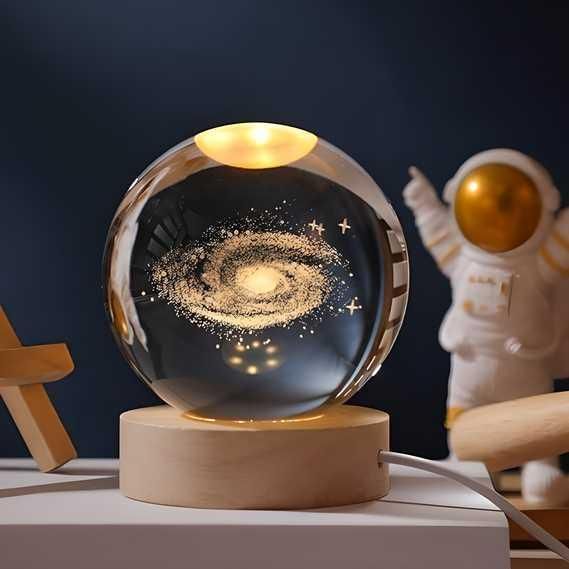 Glass ball with galaxy design on a wooden base, next to an astronaut figurine.